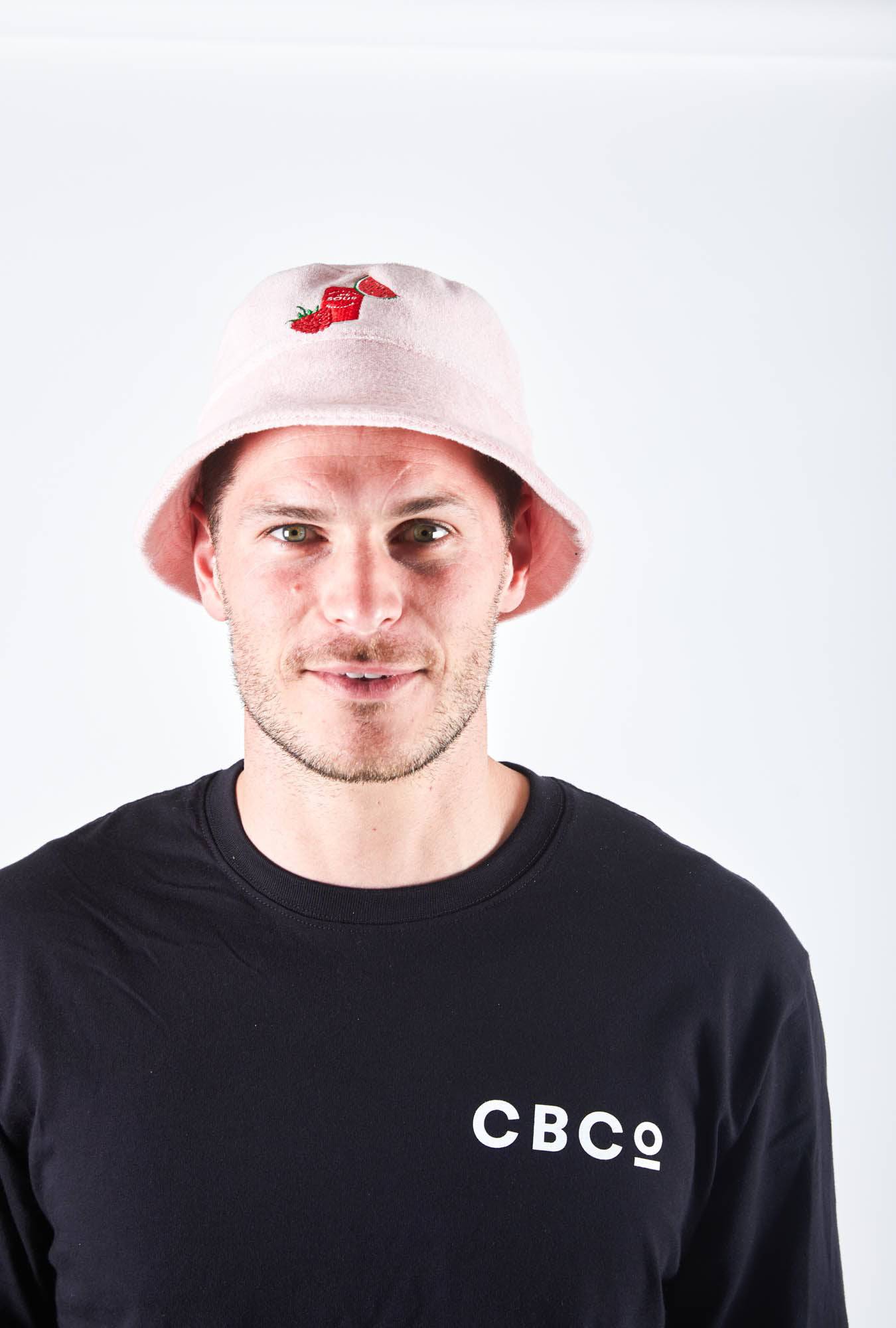 Man is wearing Colonial Brewing Co, CBCO pink bucket hat with an image of the South West Sour Beer Can, watermelon and strawberries on it. 
