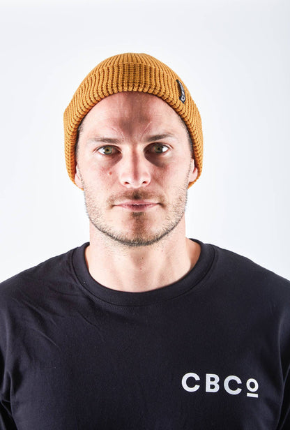 Front view of a man in a mustard-colored beanie featuring Billy Bones available at CBCO