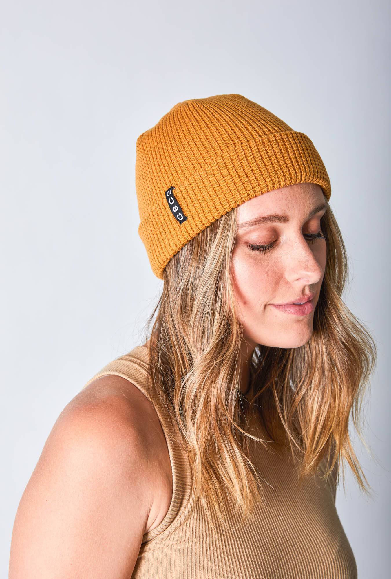 Close-up side view of a woman in a mustard-colored beanie featuring Billy Bones available at CBCO